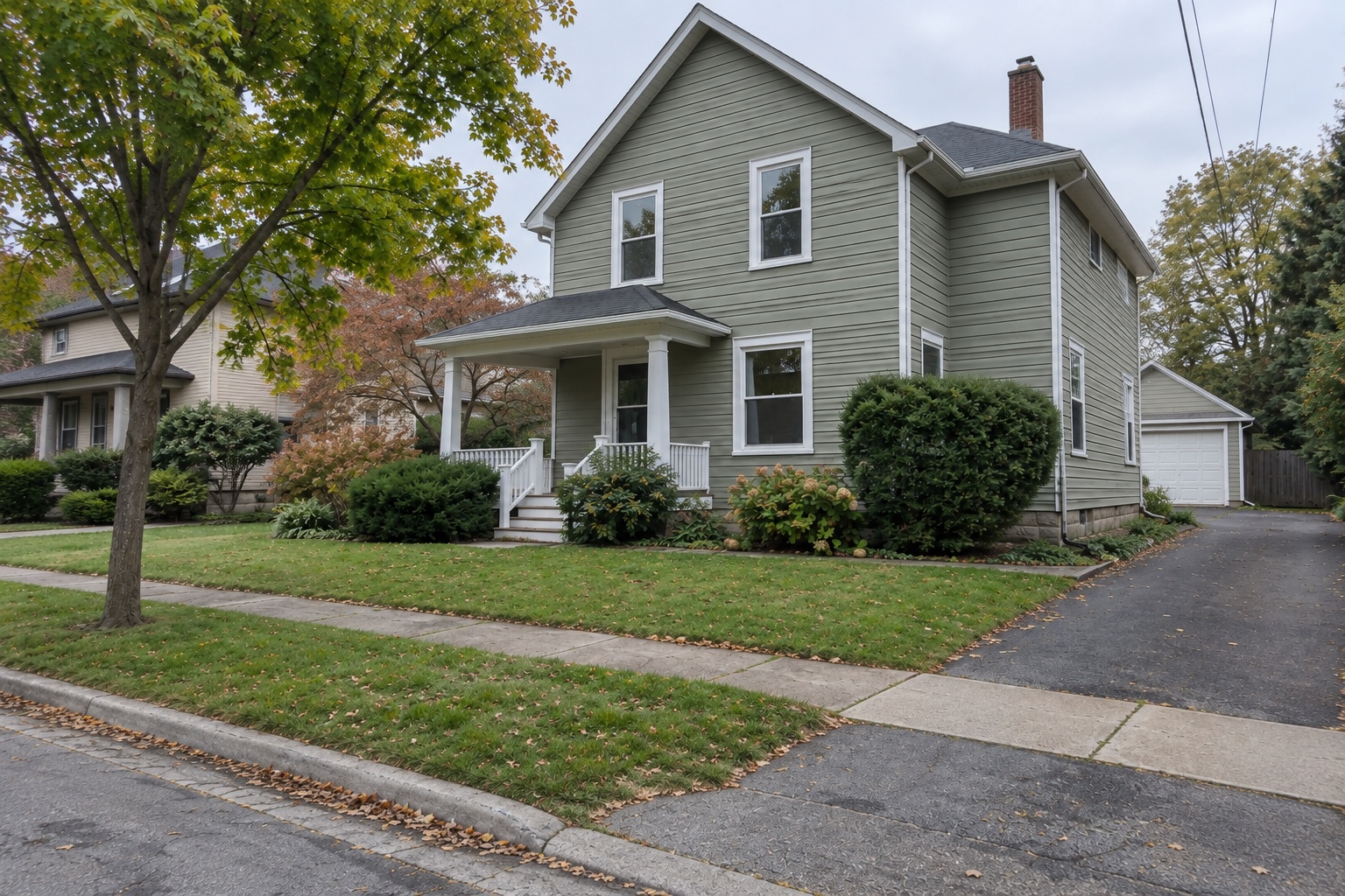 Wider front-facing view of the same house with porch, tree, driveway and neighboring context
